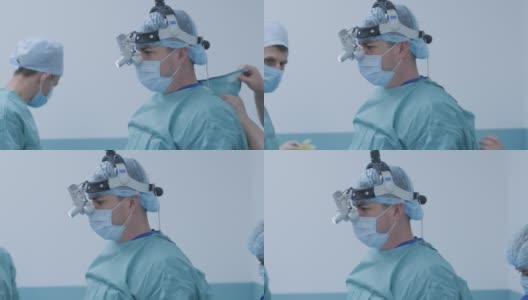 外科医生在现代化的手术室里准备手术，系无菌衣。医生配备口罩、医用头灯、手术放大镜高清在线视频素材下载