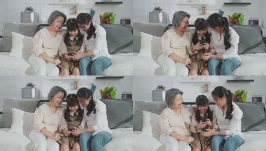 亚洲家庭的孩子，妈妈，奶奶一起在客厅玩智能手机游戏，开心地笑着。快乐活动科技生活方式手机使用概念。高清在线视频素材下载