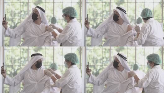一名阿拉伯穆斯林男子在诊所或医院接种新冠疫苗时通过手机自拍，护工正在注射疫苗以获得保护病毒的免疫力。人们戴着防护口罩。高清在线视频素材下载