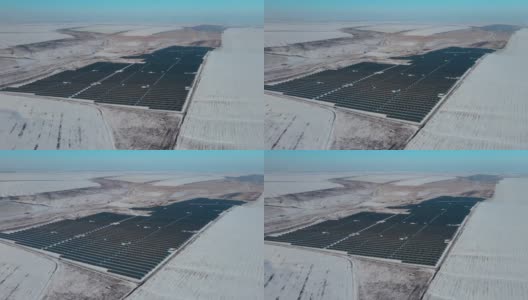 巨大的太阳能农场，蓝色的太阳能板之间的田野和小山在冬天有雪高清在线视频素材下载