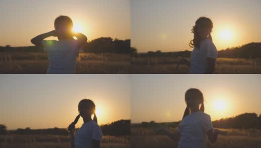 快乐的小女孩站在草地上玩着自己的头发，对着镜头。小微笑的女孩的肖像在草地上日落的背景。自由自在的概念。多莉拍摄高清在线视频素材下载