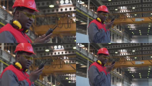 穿着防护服的年轻非裔美国工人在工厂里通过无线电通信设备交谈-放大镜头高清在线视频素材下载
