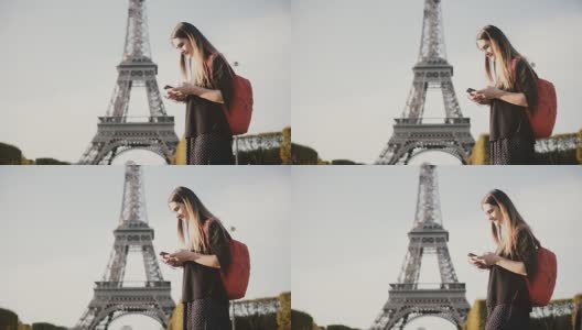 年轻漂亮的女子背着双肩包站在埃菲尔铁塔附近，用智能手机上网高清在线视频素材下载