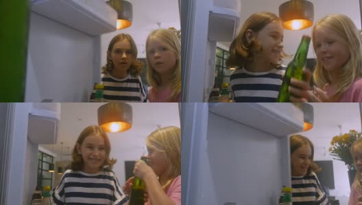 两个小女孩打开冰箱门，从冰箱里拿出一瓶绿色的汽水高清在线视频素材下载