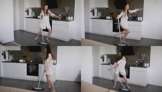 一位喜剧演员在假日打扫厨房的时候，拿着拖把跳舞，唱着歌，表演着滑稽的动作高清在线视频素材下载
