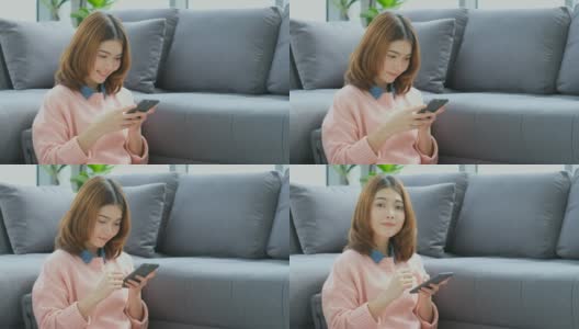年轻美丽的亚洲女人使用智能手机与幸福坐在沙发上，人们在电话，生活方式高清在线视频素材下载