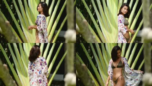 美丽的年轻亚洲女人穿着比基尼和夏季海滩和服或帕雷奥纱笼在热带花园。暑假高清在线视频素材下载