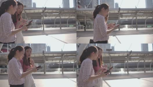 在城市里和朋友一起走路和使用智能手机的亚洲女人高清在线视频素材下载