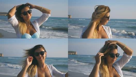 在阳光明媚的日子里，美丽的女孩穿着比基尼和衬衫沿着海岸走，玩弄她的金发。快乐的年轻女人戴着太阳镜，在海滩上享受暑假。慢动作高清在线视频素材下载