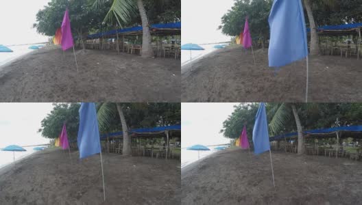 空旷的沙滩上挂着五颜六色的旗帜和遮阳伞。跟踪拍摄高清在线视频素材下载
