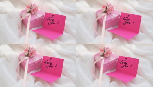 粉红色的礼盒和纸条，上面写着“我爱你”，粉红色的明信片，上面盖着白色毛茸茸的毯子。温馨的卧室细节，给爱人的早晨高清在线视频素材下载