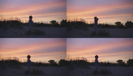 小男孩的剪影站在引人注目的紫色日落天空背景高清在线视频素材下载