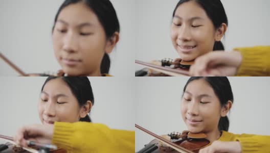 亚洲女学生穿着黄色毛衣学习拉小提琴与灰色背景，生活理念。高清在线视频素材下载