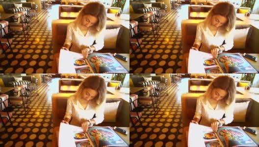 年轻漂亮的女人坐在餐馆或咖啡馆里看着菜单。高清在线视频素材下载