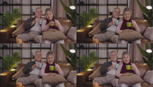 上了年纪的亚洲夫妇晚上在家里一边喝酒一边看电视上的电影。高清在线视频素材下载