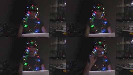 离焦点的年轻女子在笔记本电脑上庆祝圣诞节，在冬季假期的灯光，包裹在花环上。黑夜里的圣诞。假日。疲倦和期限。的焦点高清在线视频素材下载