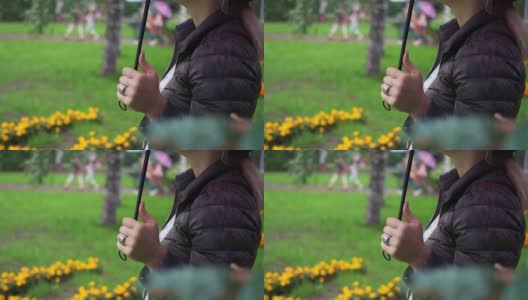 城市公园里女人拿伞的手的特写。这个城市的雨天。一个穿夹克的女人手里拿着一把伞，指甲修剪得很漂亮。手指上戴着一枚银戒指高清在线视频素材下载