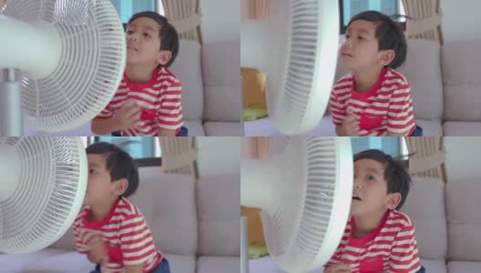 亚洲男孩站在范夏。孩子在家里享受电风扇吹来的凉风。高清在线视频素材下载