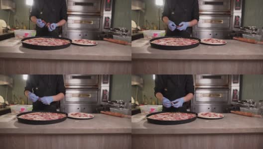 厨房里的厨师在做美味的意大利披萨。戴手套涂抹意大利香肠。高清在线视频素材下载