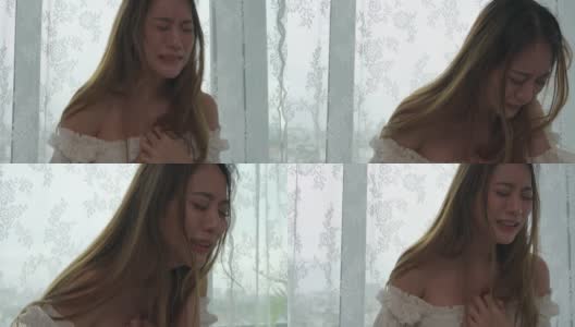 4K沮丧美丽的亚洲女人独自站在公寓房间的窗口哭泣和尖叫。孤独悲伤的女孩，想起悲伤烦恼。消极情绪与心理健康的概念。高清在线视频素材下载