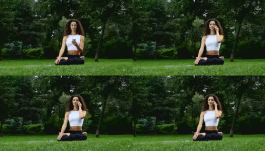 年轻女子在公园里练瑜伽，一边讲电话高清在线视频素材下载