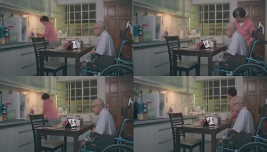 坐在轮椅上的亚洲老人和妻子在晚餐后的闲暇时间在厨房用平板电脑给家人视频通话高清在线视频素材下载