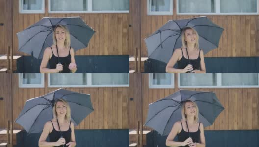 迷人的金发女郎在下雨时撑着伞。一个在夏日淋浴的女人高清在线视频素材下载