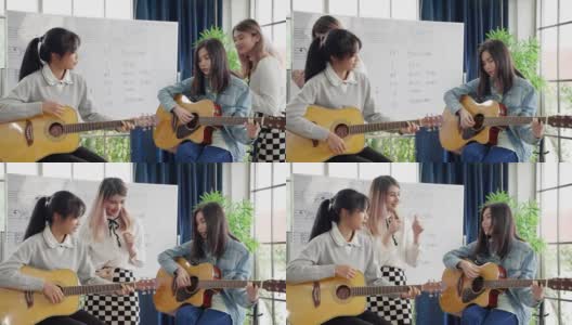 在一所音乐学校的课堂上，一位年轻的亚洲音乐老师正在教学生读乐谱和正确的吉他和弦高清在线视频素材下载