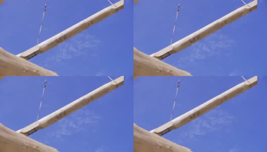 起重机在蓝天的背景下吊起横梁。夹。建筑工地的起重机将经过重处理的木材运送到建筑工地高清在线视频素材下载
