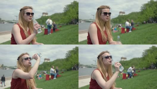 夏日里，戴着太阳镜的年轻女子从塑料瓶里喝水高清在线视频素材下载
