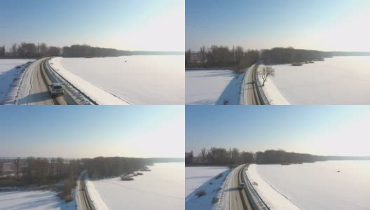 航拍的汽车行驶在冰雪覆盖的道路附近结冰的湖。冬季，白色越野车行驶在大坝路线上。飞过汽车，驶过河桥。风景优美的景观。俯视图高清在线视频素材下载