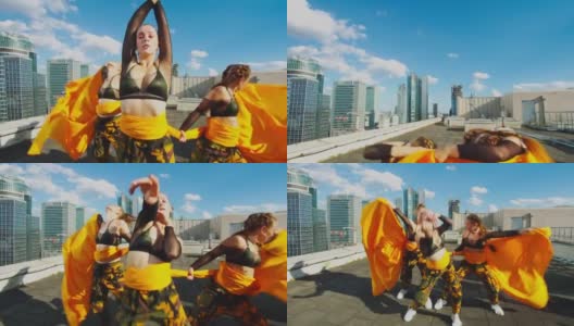 身穿迷彩服的女舞者在阳光明媚的屋顶上一起表演。橙色织物的现代编舞高清在线视频素材下载