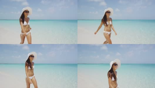 海滩度假女人在阳光下微笑快乐的夏天假期在热带海滩。美丽的多种族亚洲华人/白种人比基尼模特，戴着沙滩帽。高清在线视频素材下载