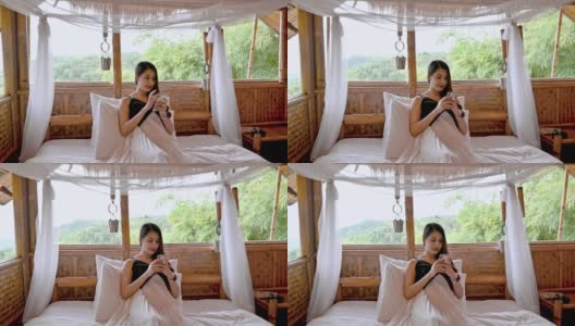 亚洲女人在木制小屋的床上用智能手机度假高清在线视频素材下载