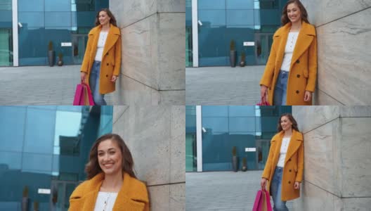 商务女拎着购物袋，身穿黄色外套，走在公司大楼门外背景高清在线视频素材下载