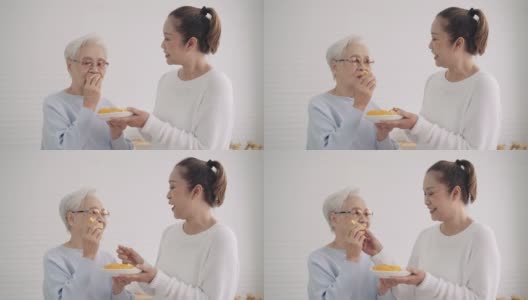 中女儿让她的亚洲年长的母亲在厨房准备水果奶昔之前尝一小块橘子，享受周末的活动，前面的景象，年长的生活方式高清在线视频素材下载