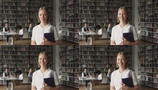 美丽的微笑少女持有文件夹在大学图书馆摆姿势高清在线视频素材下载
