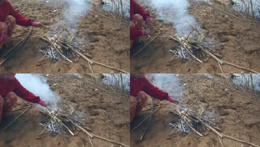 妇女在烤鱼下添加小树枝以保持炉火燃烧高清在线视频素材下载