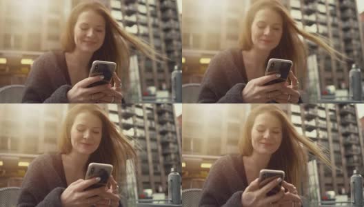 漂亮的红头发女人坐在长凳上微笑着使用智能手机，连接女孩写信息。华丽的纽约城市景观的背景。高清在线视频素材下载