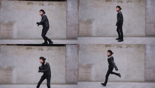 一名留着小胡子的中国青年在城市混凝土墙旁的街道上跳舞。他穿着夹克，看起来有点笨拙，4k镜头，慢动作。高清在线视频素材下载