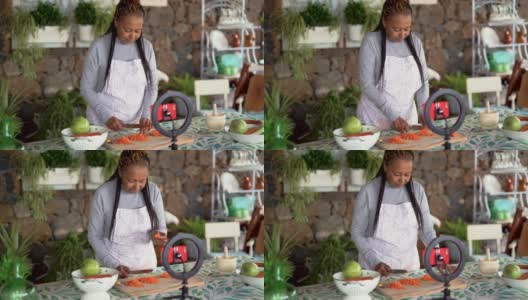 快乐的非洲资深女性用智能手机在网上直播，并引领着户外烹饪高清在线视频素材下载
