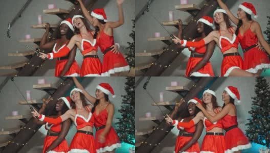 欧洲、亚洲和非洲的年轻女孩穿着红色的新年衣服，戴着帽子，在圣诞树前跳舞，微笑着用手机拍照高清在线视频素材下载