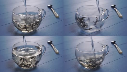 将沸水倒入一个透明的玻璃杯中，杯底是蓝色的木质背景上的花草茶花瓣高清在线视频素材下载