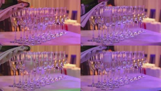 侍者将香槟倒入玻璃杯中，香槟玻璃杯放在自助餐桌上，餐厅或酒店的大厅里，侍者的手上戴着白手套拿着一瓶香槟，室内，特写高清在线视频素材下载