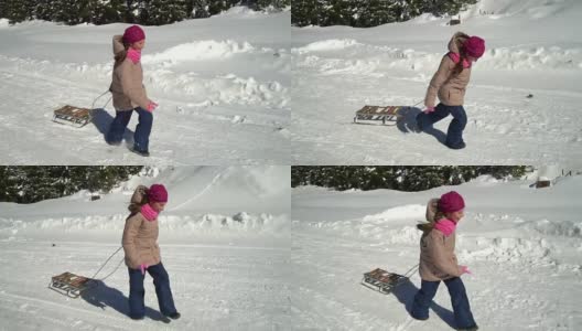 一个快乐的女孩在冬天的山上跑过一片雪林。她是笑。她身后拖着雪橇。缓慢的运动。高清在线视频素材下载