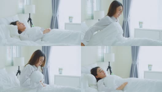 亚洲美丽生病的女孩在睡衣起床在卧室。有魅力的年轻女性在床上醒来后会感觉很难受，肚子疼或者早上抱肚子。高清在线视频素材下载
