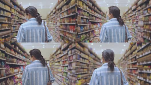 年轻的成年亚洲女性戴着防护口罩，在百货商场精心挑选新鲜产品或消费产品，欢快的新常态购物生活方式。高清在线视频素材下载
