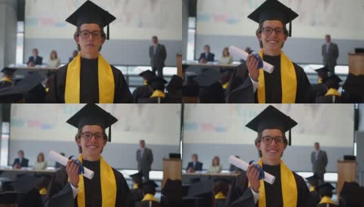 年轻英俊的男学生在毕业典礼上手持隐藏的毕业证书，对着摄像机微笑高清在线视频素材下载