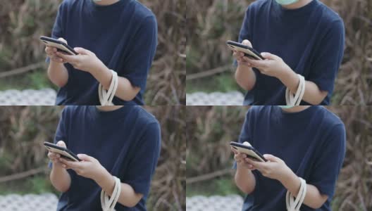 亚洲女性戴着防护面具在户外花园玩智能手机放松高清在线视频素材下载