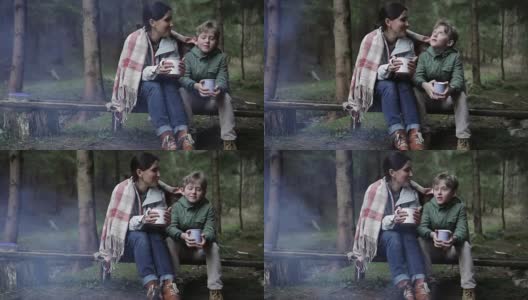母亲和儿子坐在包裹在格子的篝火前，喝着茶高清在线视频素材下载